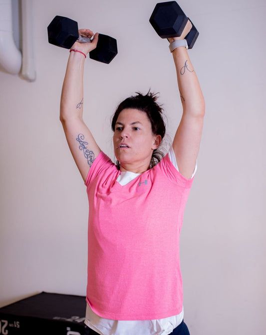 Daša lifting two dumbbells overhead during a strength workout