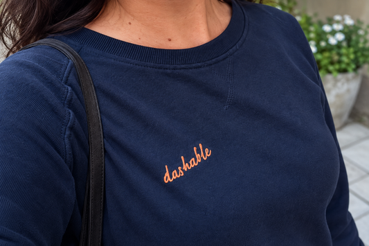 Close-up of a navy Dashable sweatshirt with an orange embroidered logo
